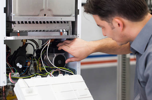 An HVAC technician inspects internal components and wiring inside a furnace during a repair service.