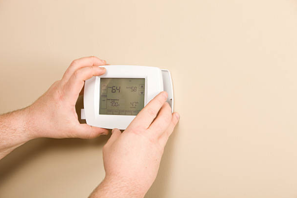 Person adjusting a digital thermostat on an interior wall to manage home heating and cooling settings.