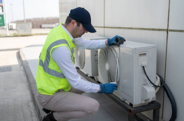 An HVAC technician inspecting and servicing an outdoor air conditioning unit.
